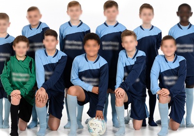 A group of young boys wearing colorful soccer uniforms, smiling and posing together on a grassy field.