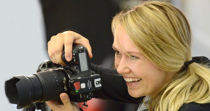 A woman smiles brightly while holding a camera, ready to capture moments.