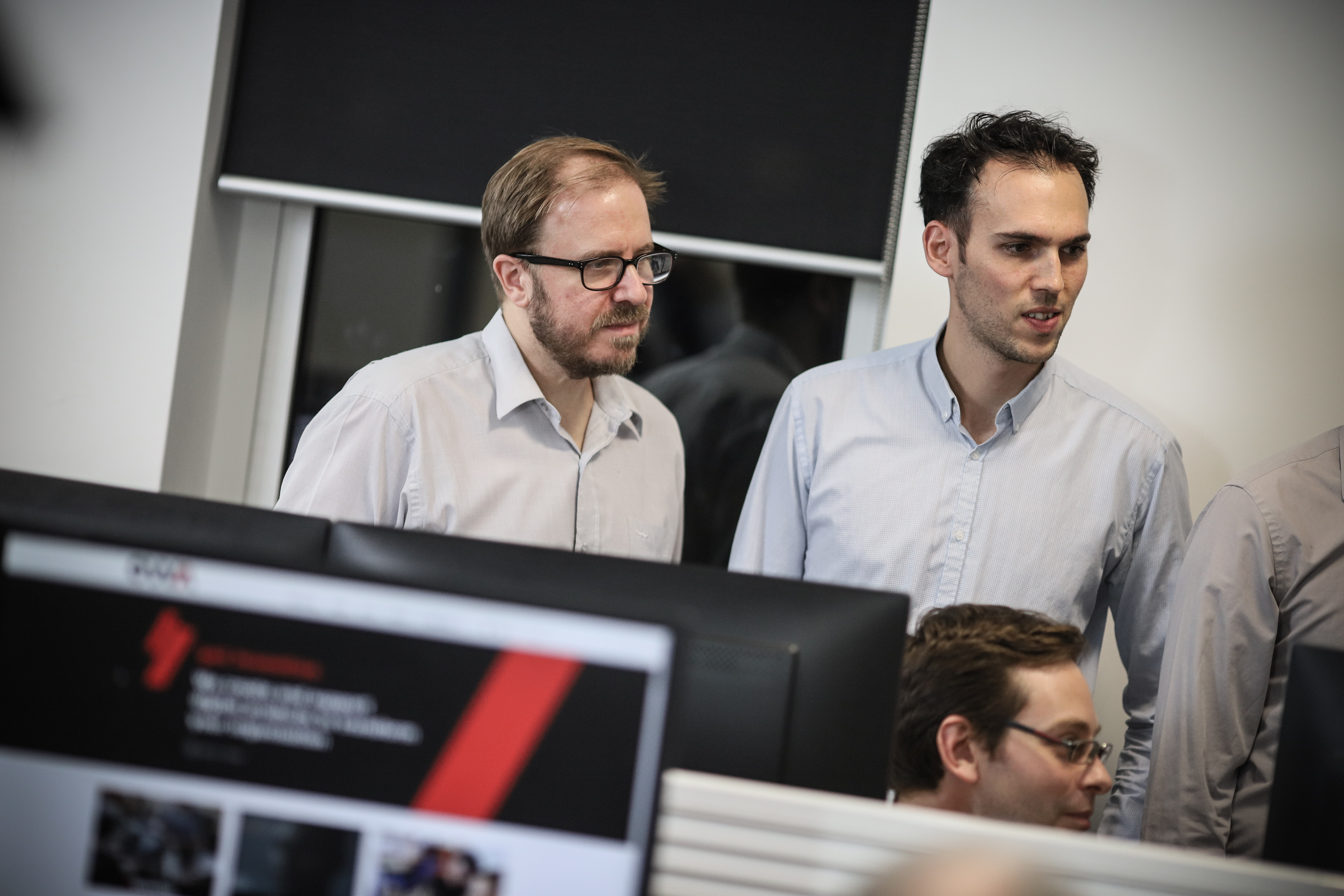 Two OWA team members discussing legacy system support while standing in front of a computer screen displaying technical information