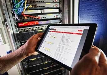 OWA team member holds a tablet in front of a server rack, illustrating Web Application Development in a tech environment.