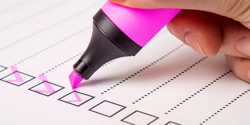 A person writes a checklist with a pink pen, focusing on tasks related to Web Application Development
