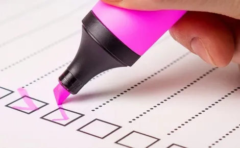 A person writes a checklist with a pink pen, focusing on tasks related to Web Application Development