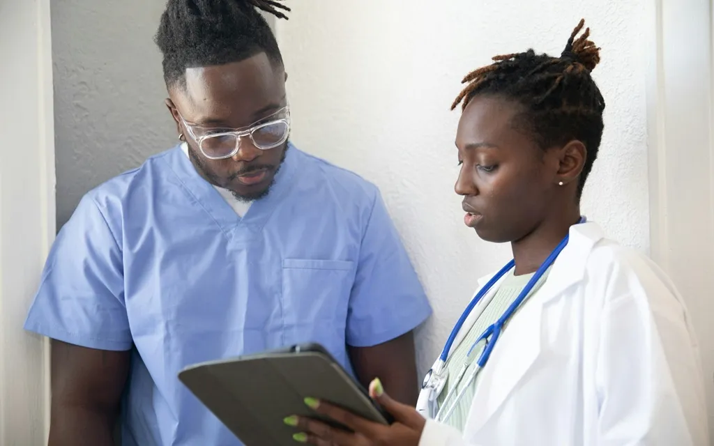 A male doctor and a female nurse reviewing information together on a tablet in a medical setting.