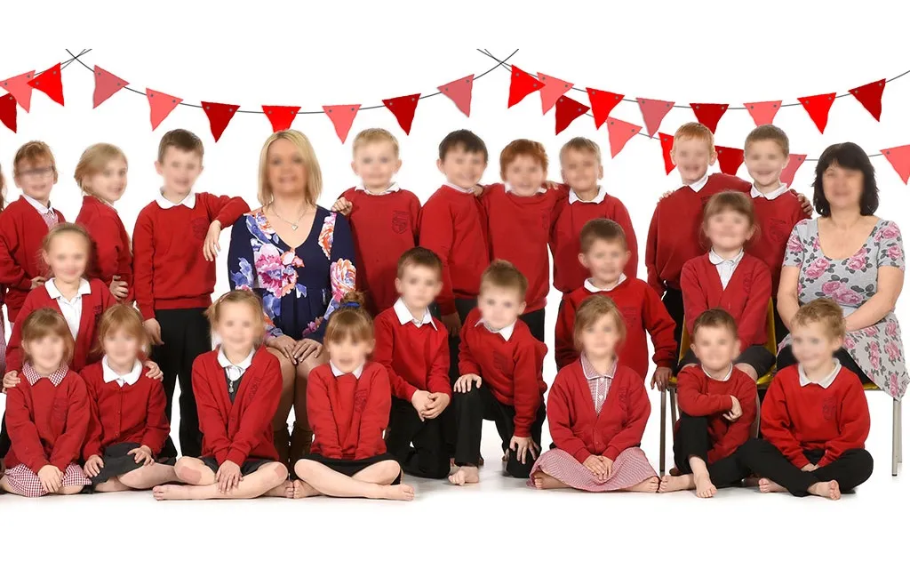 A group of children wearing red school uniforms, smiling and standing together in a playground setting.