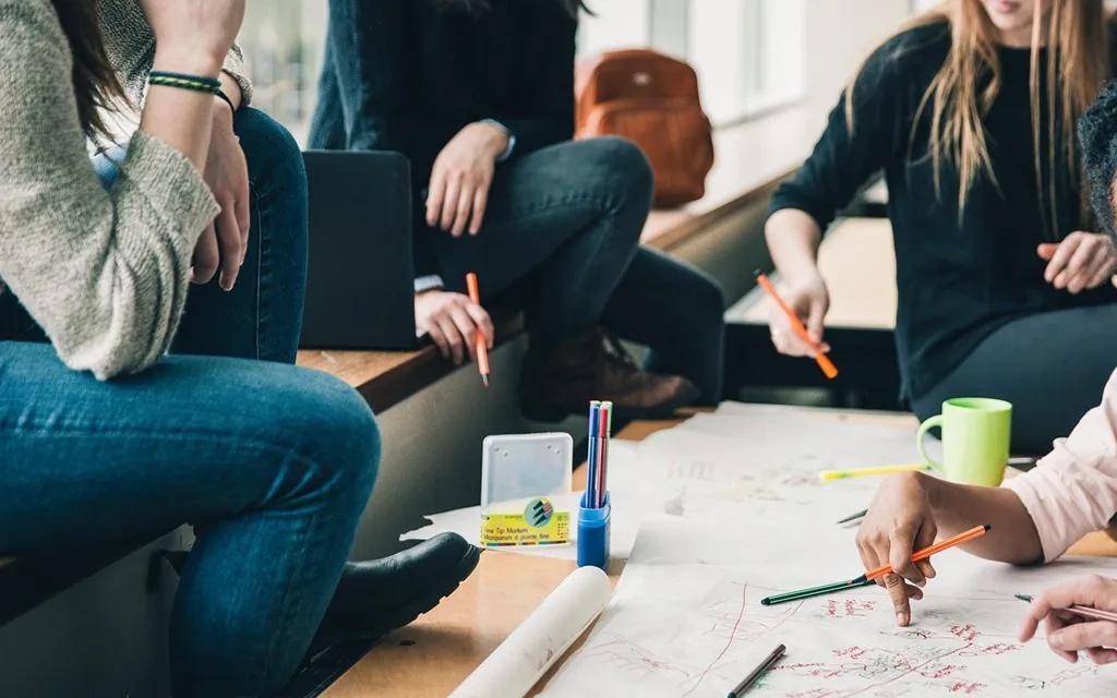 A diverse group of people gathered around a table, engaged in discussion while examining a drawing.