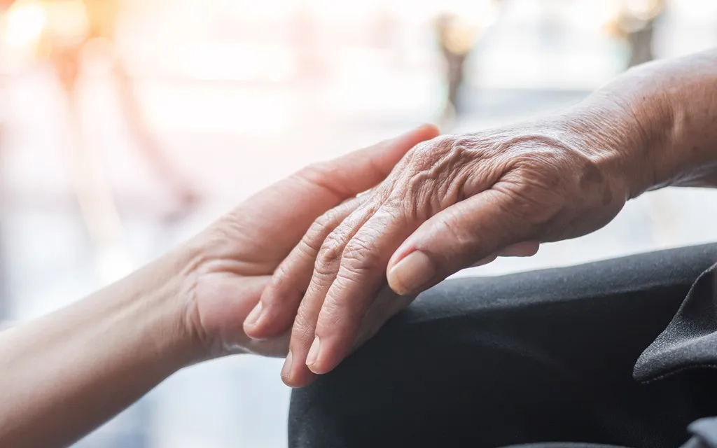 An elderly person gently holds the hand of a younger individual, symbolizing connection and support.