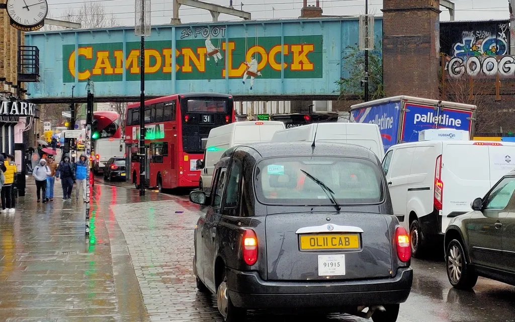 A vibrant street scene in Camden Town, London, showcasing a mix of cars, buses, and taxis in heavy traffic.
