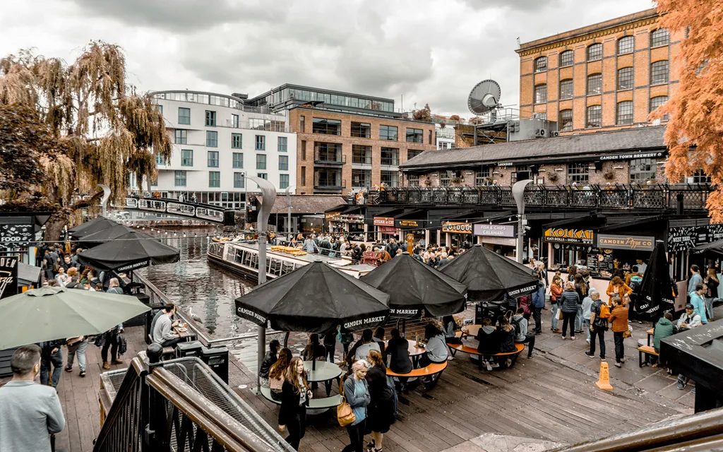 People walking along a canal in Camden Town, London, surrounded by shops and lively city scenery.