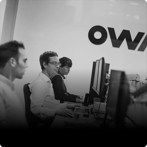 OWA team members working on computers in front of a company logo, focused on their tasks.